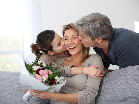 Mor der bliver forkælet på Mors Dag af sin mand og datter, med blomster og kys